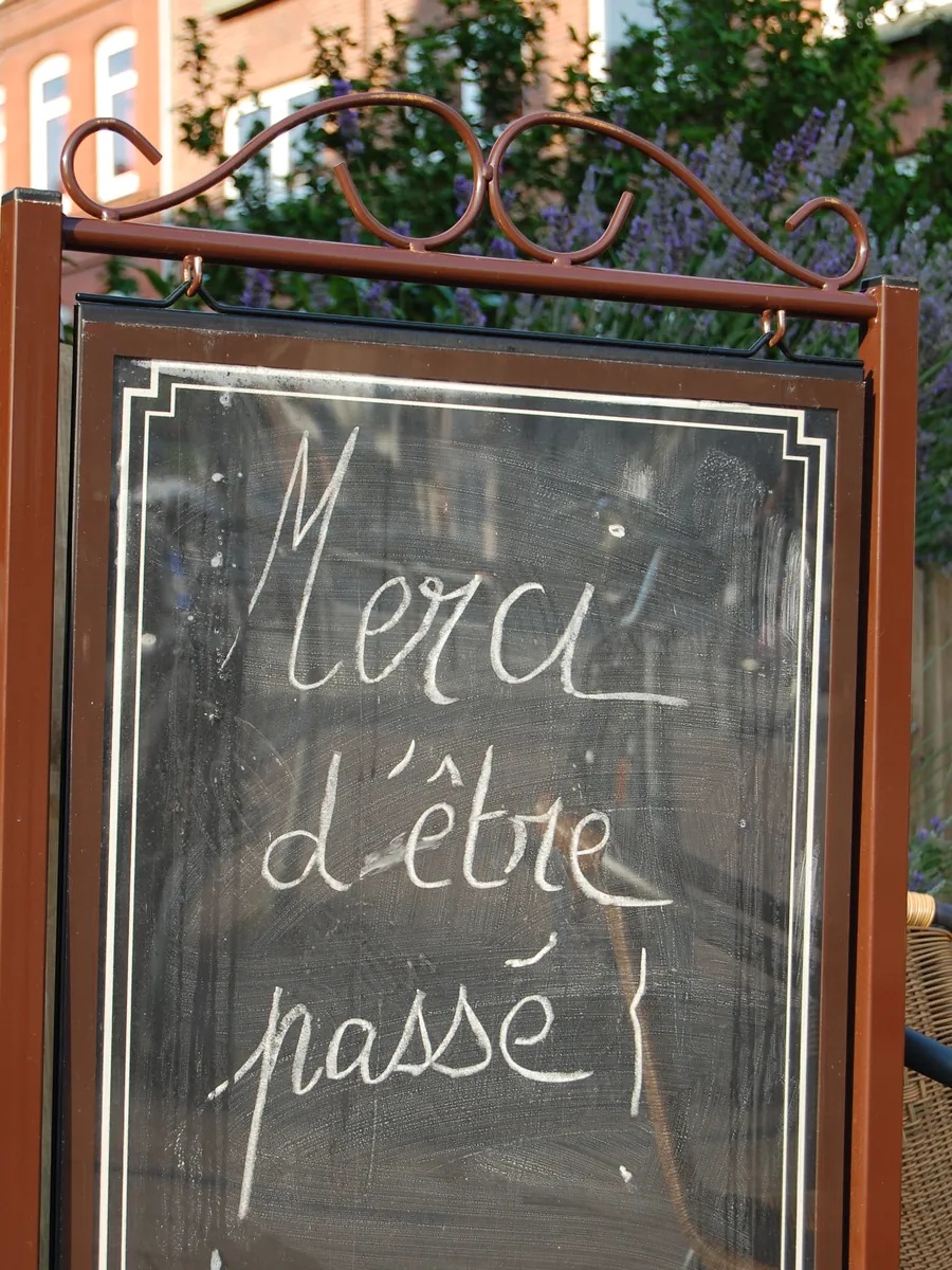 Kreidetafel „Merci d'être passé!“ in einem verschnörkelten Metallrahmen