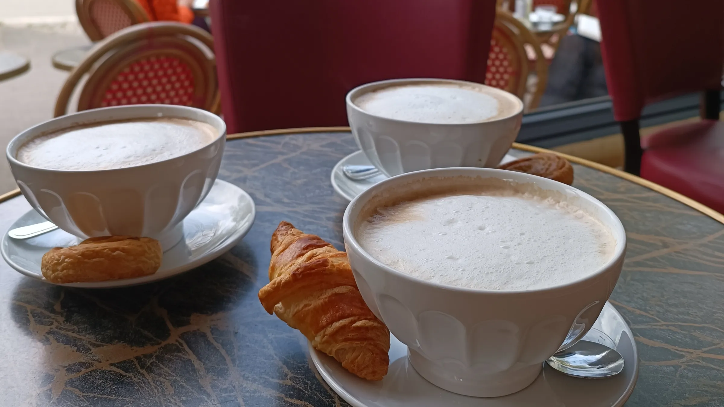 Milchkaffee in weißen Schalen und ein Croissant auf dem Marmortisch am Fenster, draußen die Terrasse