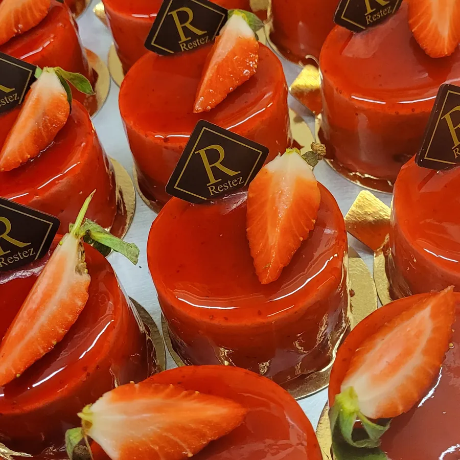 Rote Törtchen mit Erdbeerhälfte und Restez!-Plättchen in Reihen auf dem Blech