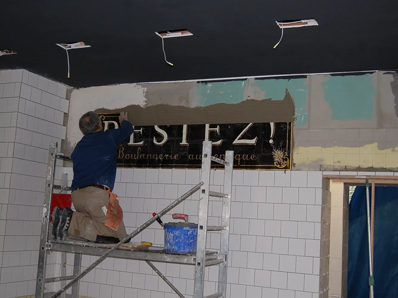 Baustelle im Laden: ein Handwerker auf dem Gerüst vor dem Restez!-Schild an der gefliesten Wand