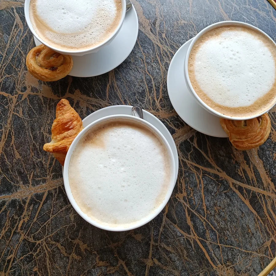 Drei Milchkaffees mit kleinen Croissants auf einem Marmortisch, von oben