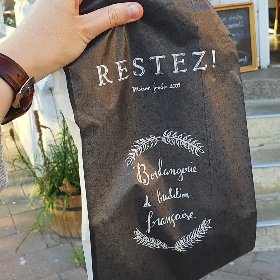 Eine Restez!-Tüte mit dem Aufdruck Boulangerie de tradition française vor dem Laden